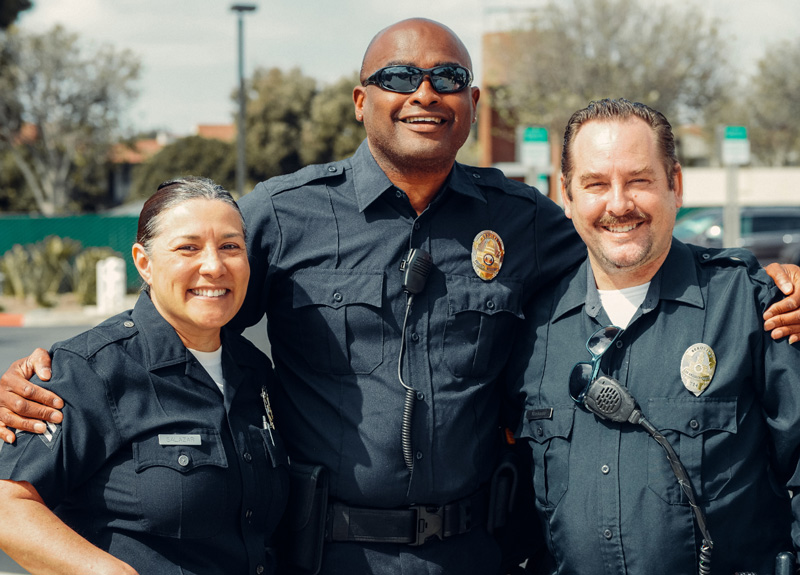 3 police officers stand together smiling at the camera while wearing their uniforms.