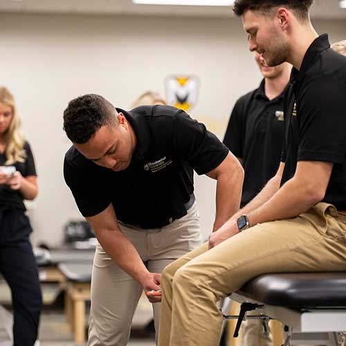 Two students practice checking on another's reflexes on the knee as a class demonstration