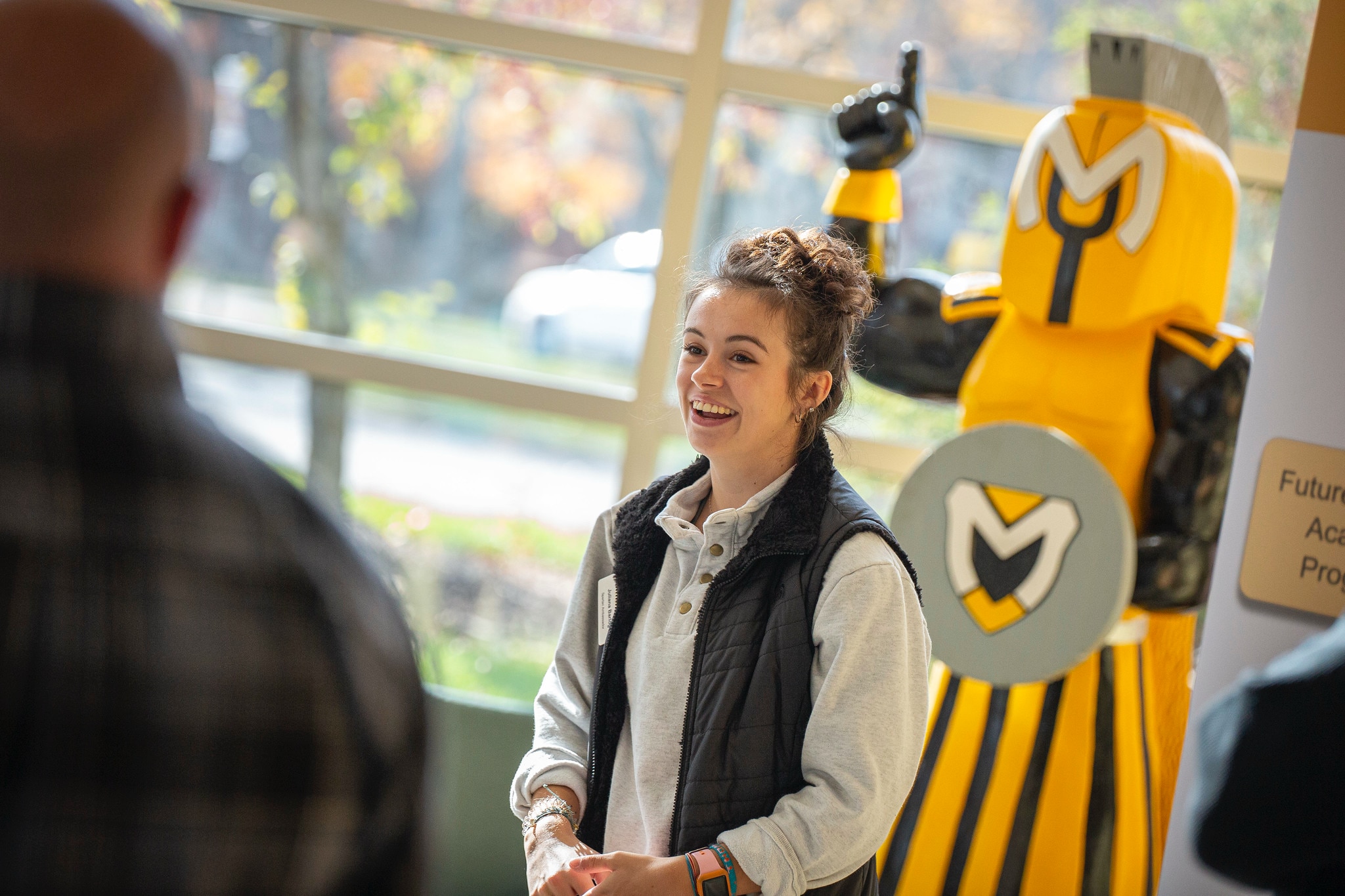 student giving a tour on a visit day inside with mascot in background