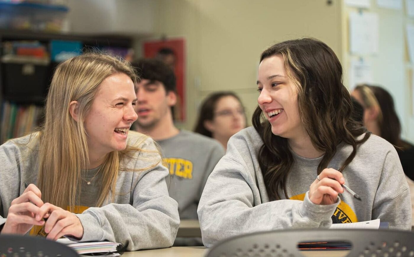 Education class inside with two female students smiling at each other Education class inside with two female students smiling at each other