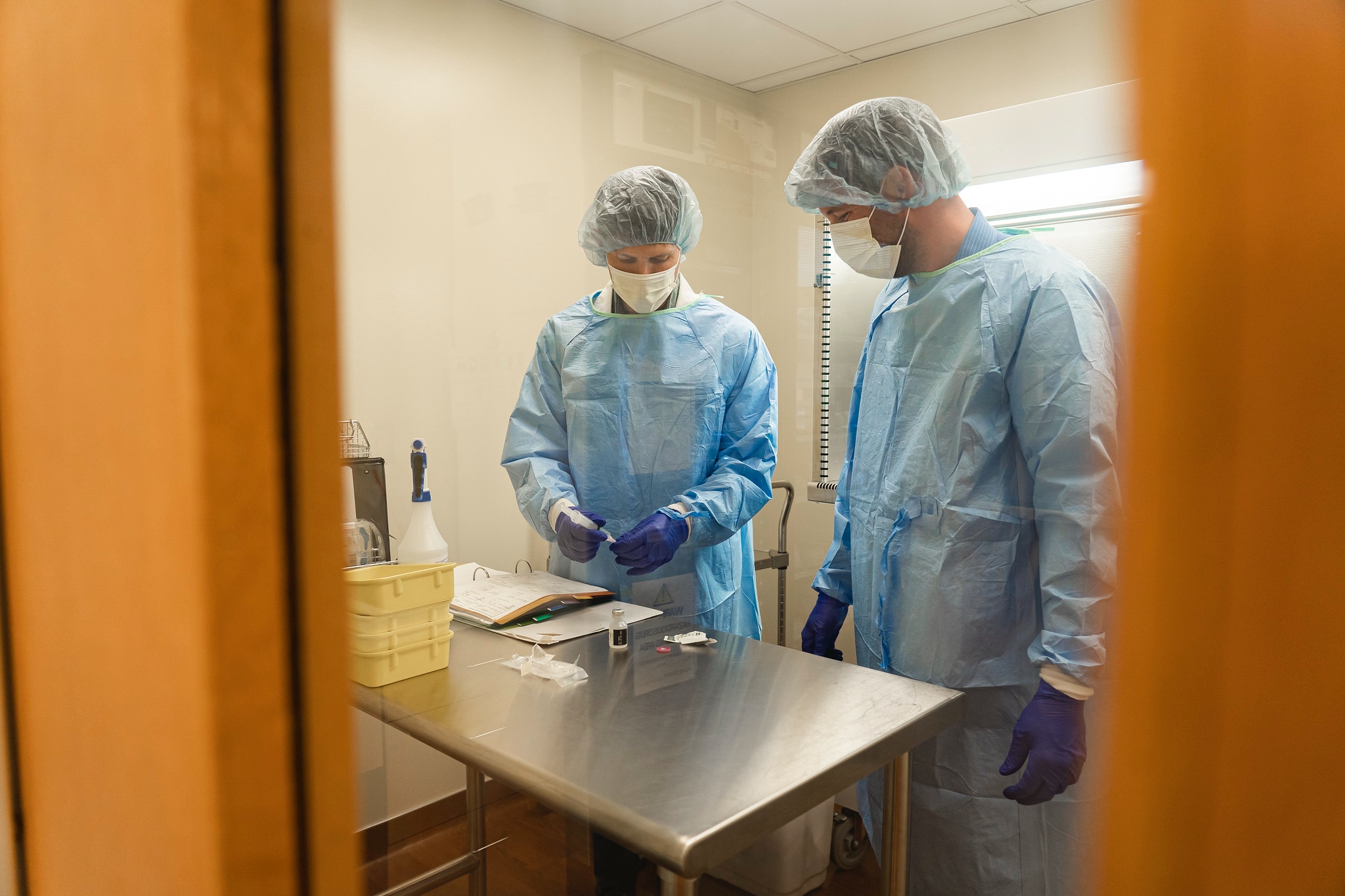 two pharmacy students study a medication in gloves, hairnets, and masks