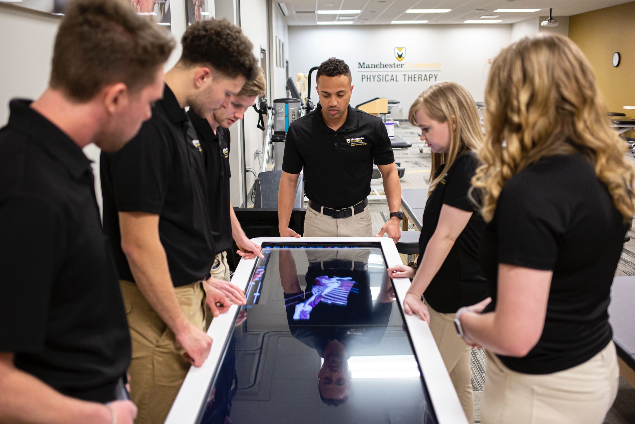 a group of physical therapy students look at a computer screen as another student controls the computer
