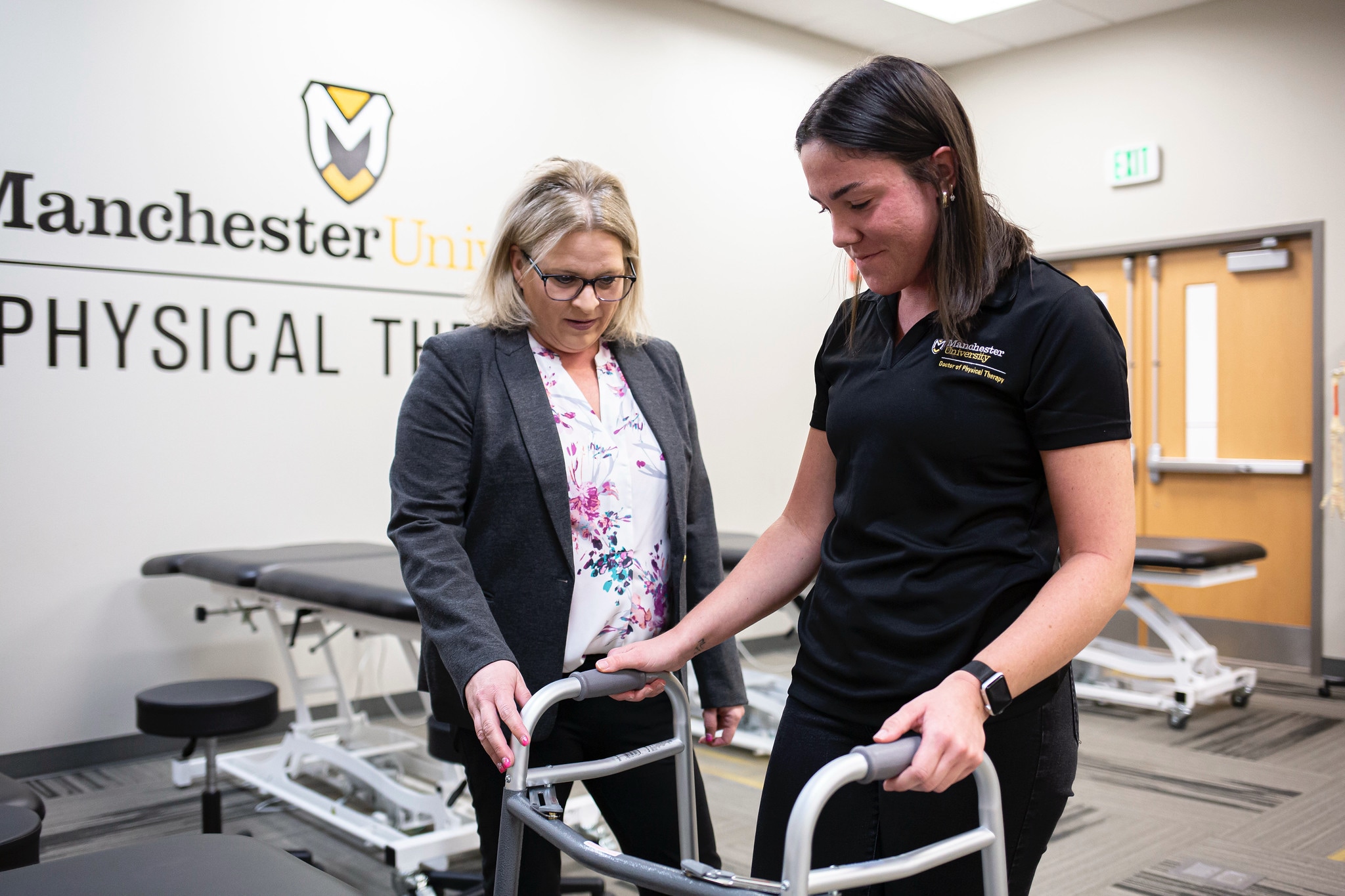 a female student walks with a walker as a professor watches in a physical therapy classroom