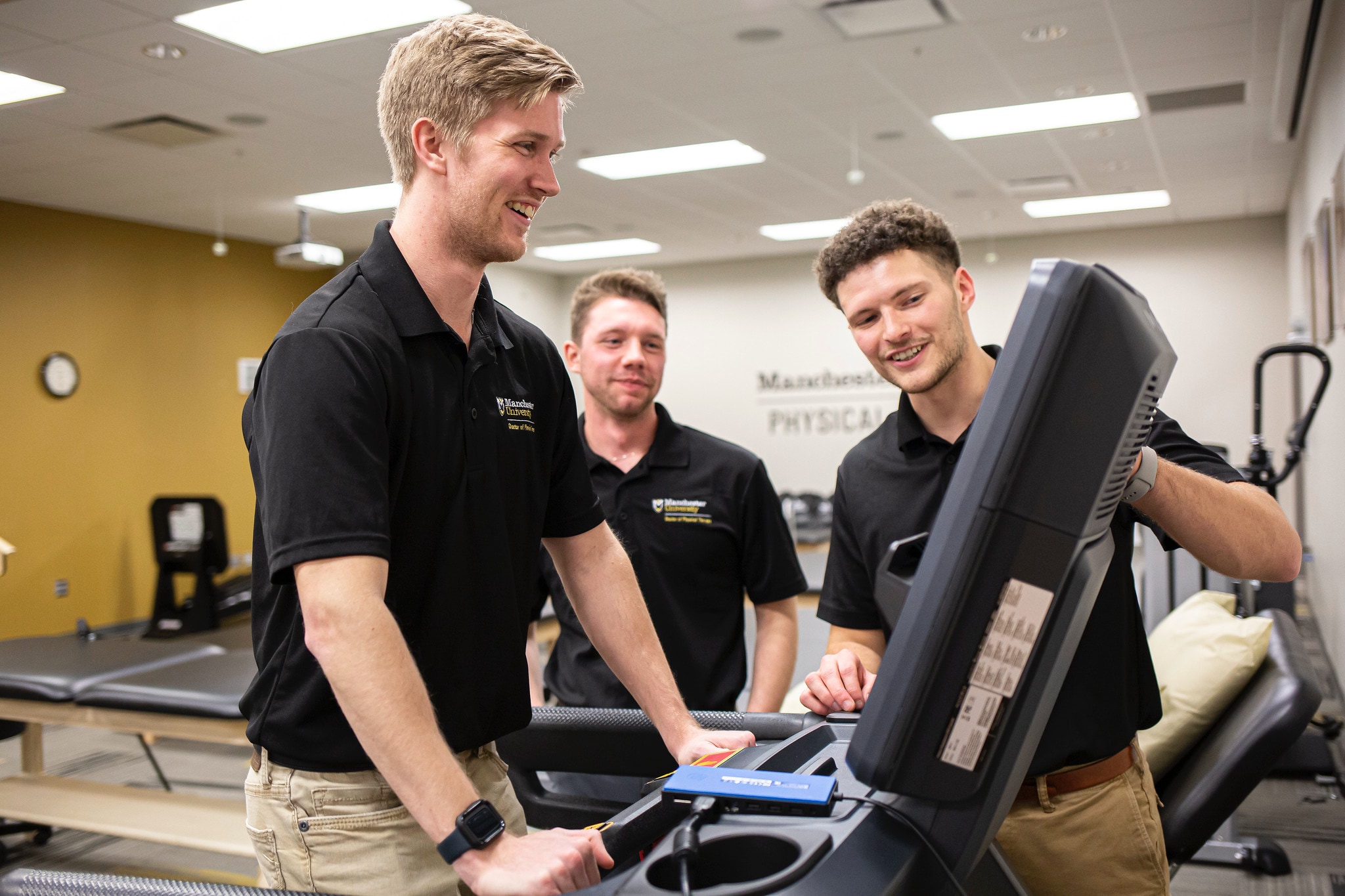 physical therapy students wearing polos looking at the screen of a treadmill