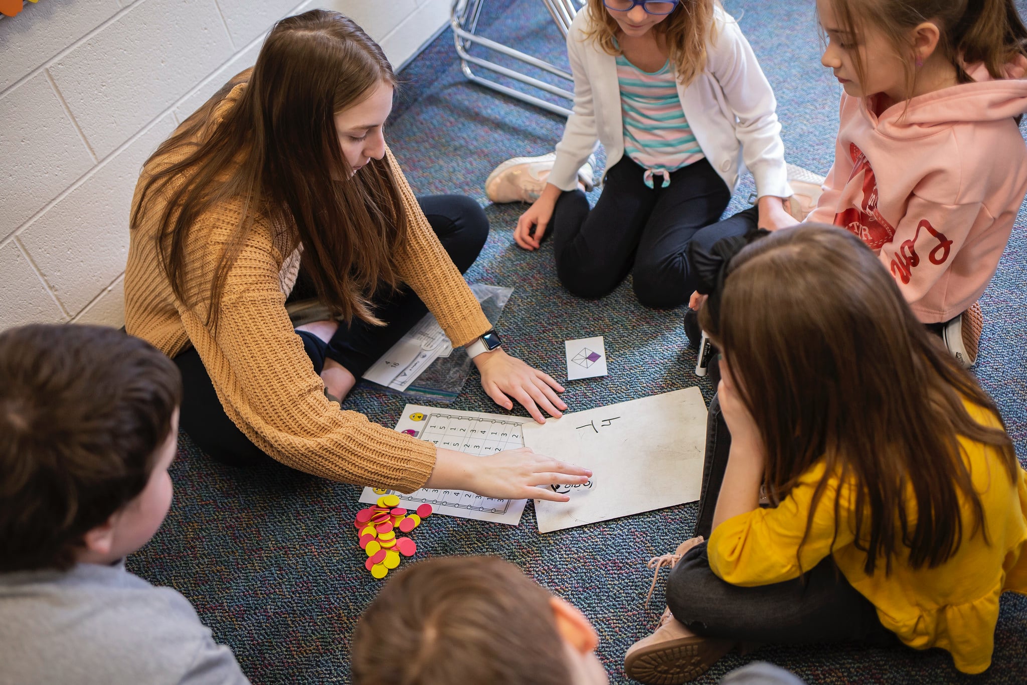 a manchester student teacher sits on the floor and explains an activity to a group of elementary students