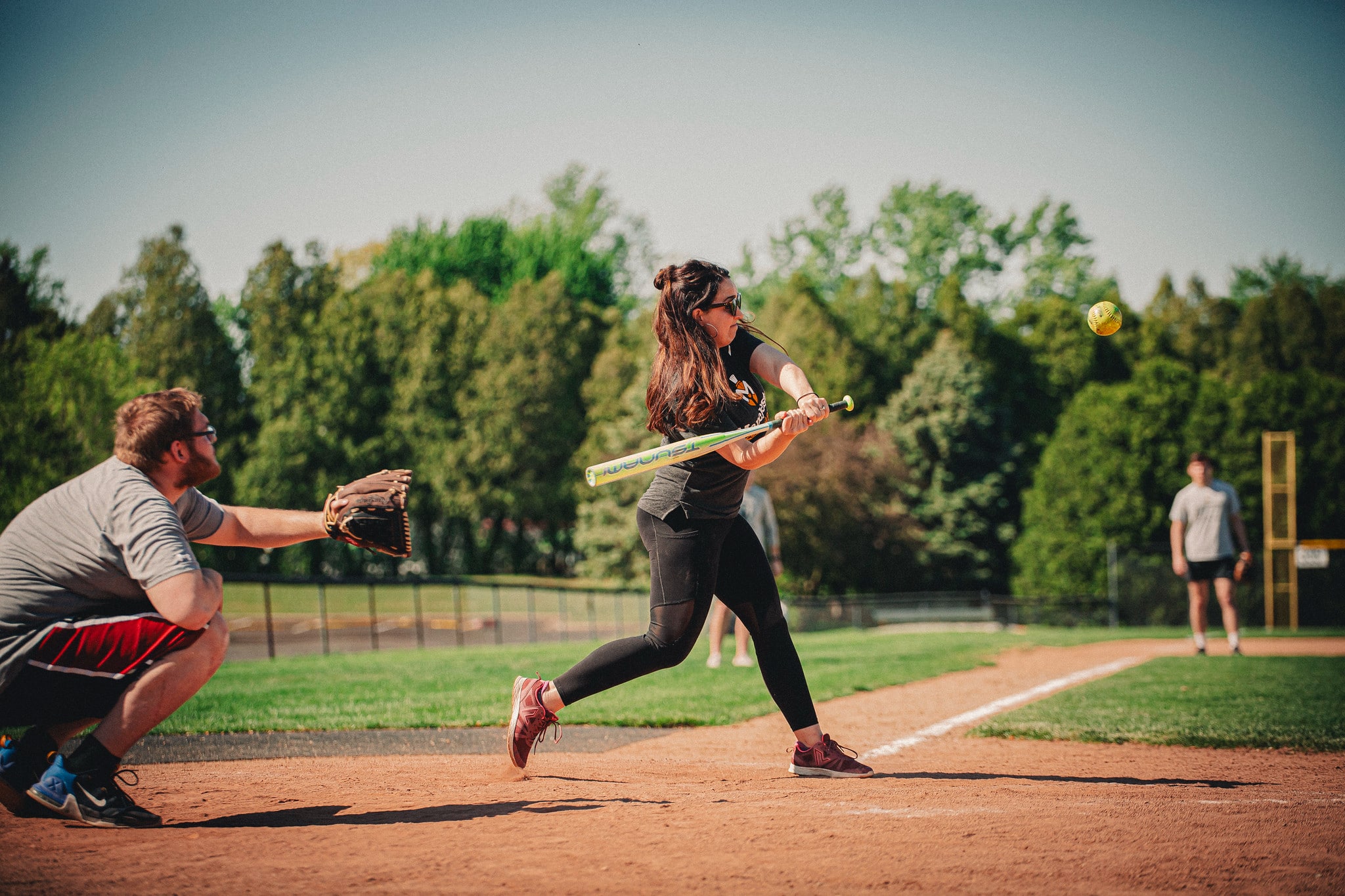 female student swings at a softball while a male students prepares to catch the pitch