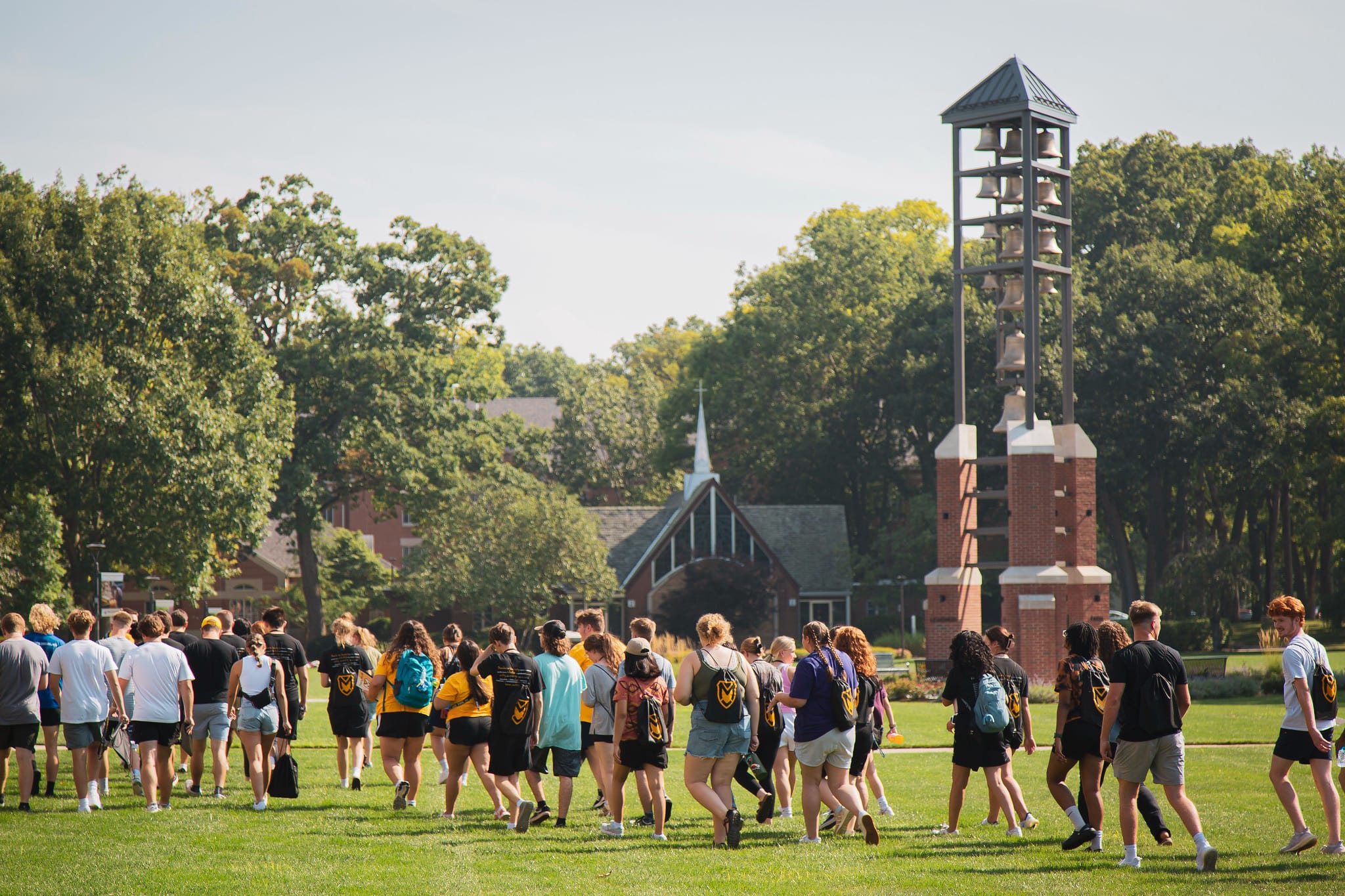 WeekOfWelcome-12 Manchester University students walking across an open grassy area in front of a bell tower