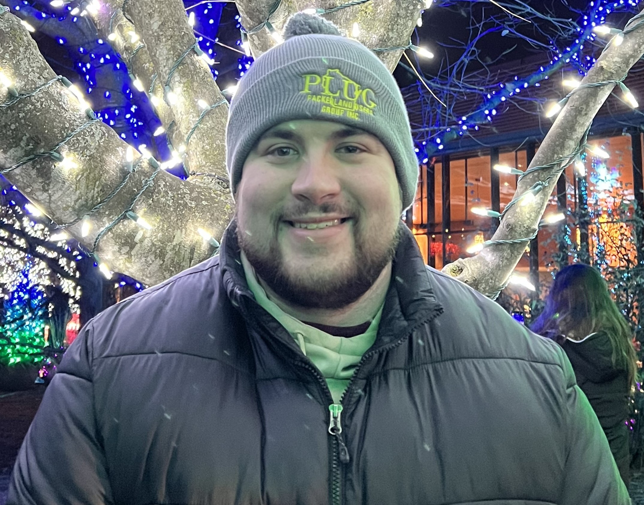 Chris Brunstetter in winter jacket and hat while standing in front of tree with lights
