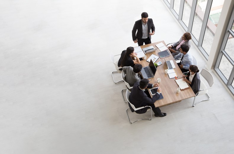 Group of people in business attire seated at a table with laptops and tablets