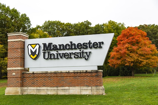 Manchester University sign in front of tree with red leaves during autumn