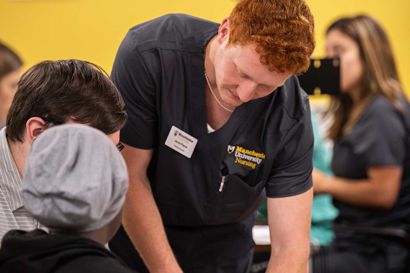 Male nursing student in scrubs talks to two people