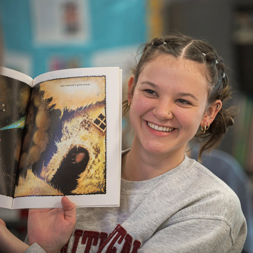 As part of an experiential learning opportunity, a student is reading a children's book during a role play.