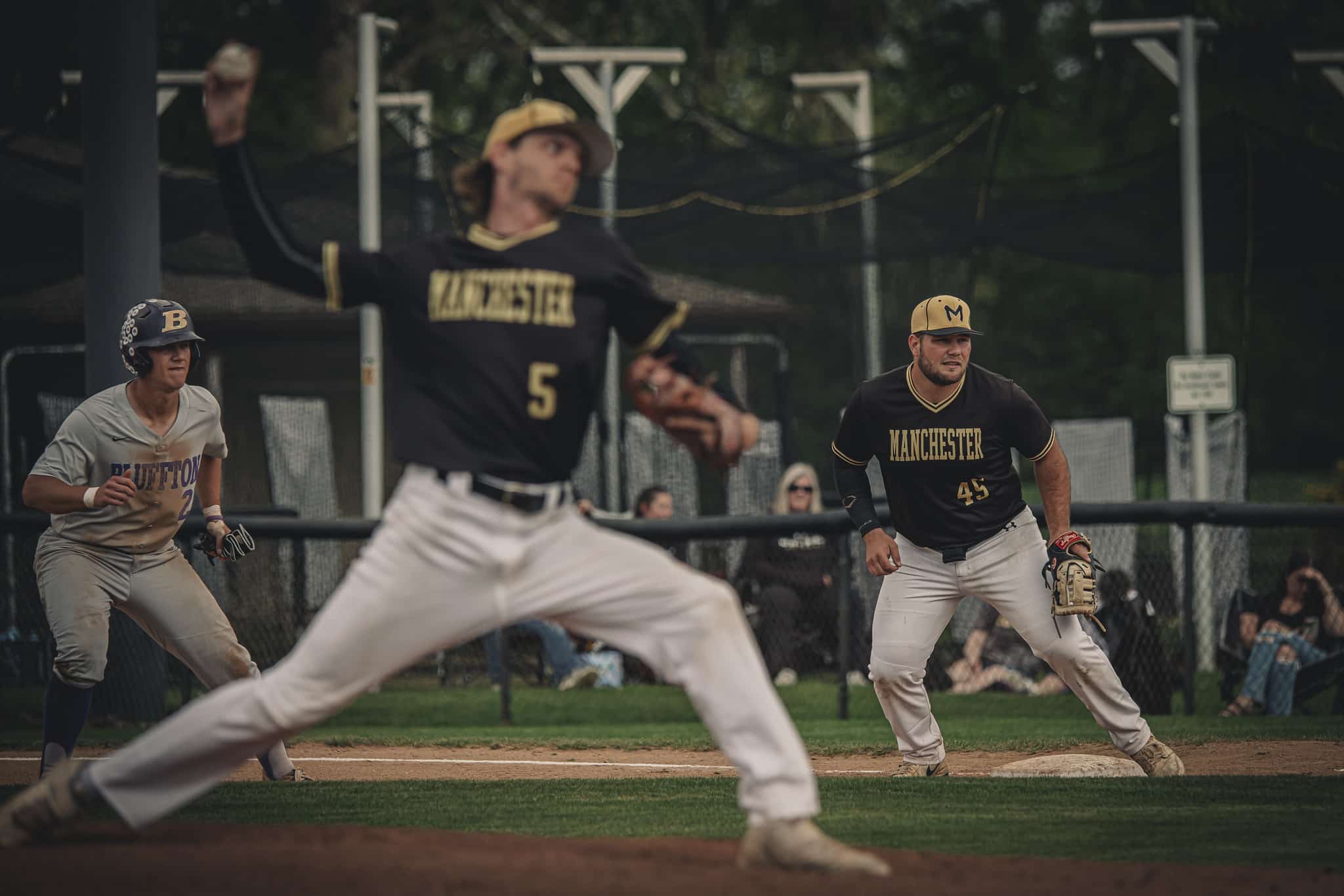 Manchester University pitcher throws baseball as first baseman prepares for the play