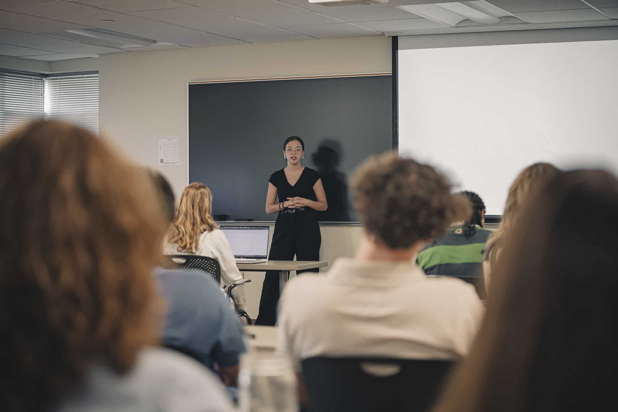 Another female presents in the classroom in a black pants-suite.