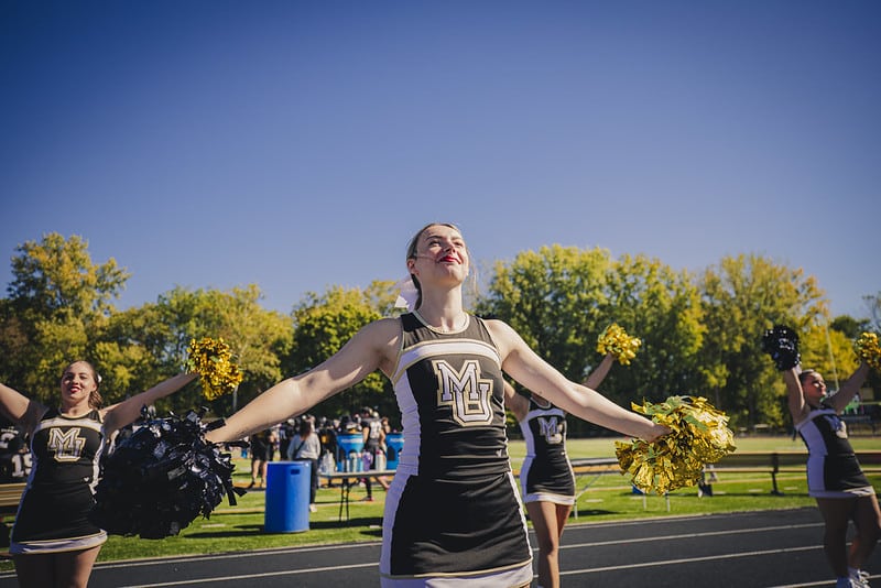 A solo cheerleader waves her black and gold pom poms to the crowd
