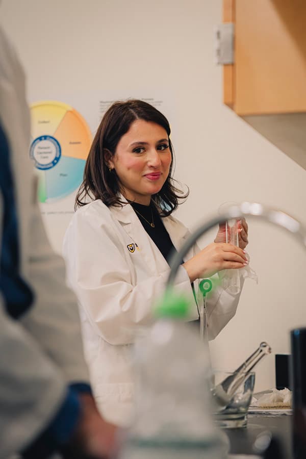 A female student in a white lab coat participates in the distance pathway lab.