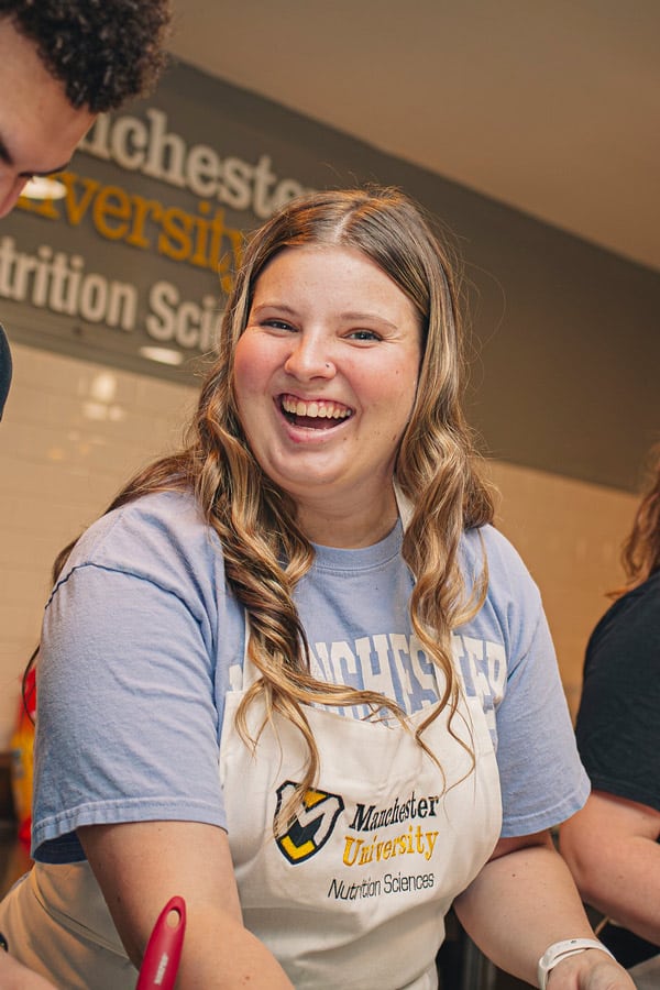 A female student wearing an apron in the MSNGx Lab smiles while making a tasty treat.