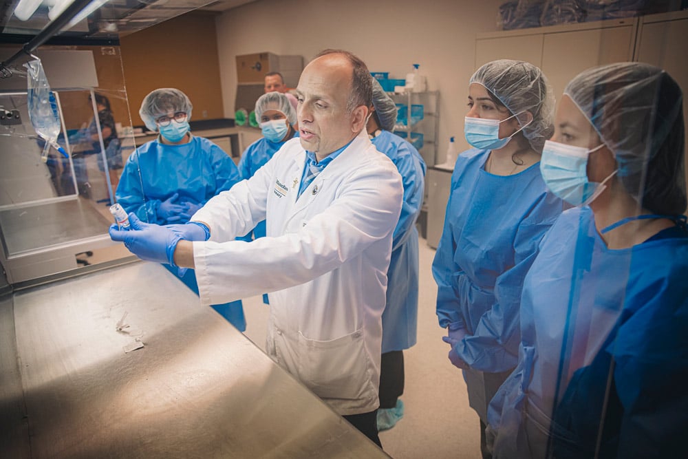 An MU instructor demonstrates proper usage with a vial and syringe in front of students in blue scrubs