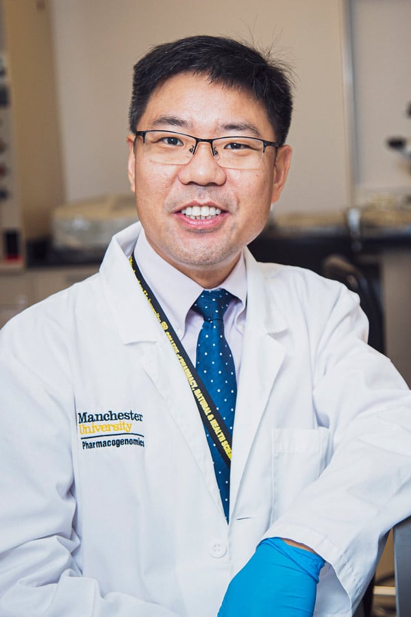A PGx instructor stands in the lab posing with a smile in a white lab coat.