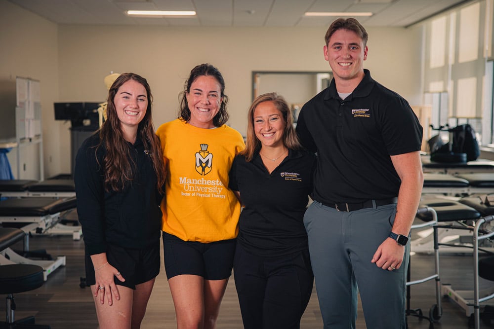 Four students smile for a photo with DPT equipment in the background.