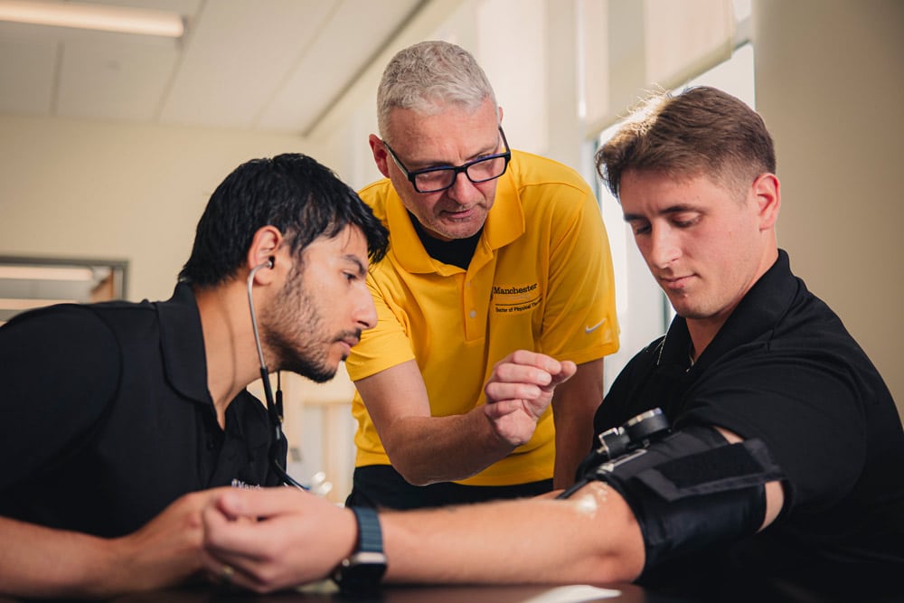 a professor at MU engages with 2 students using a blood pressure monitor. 