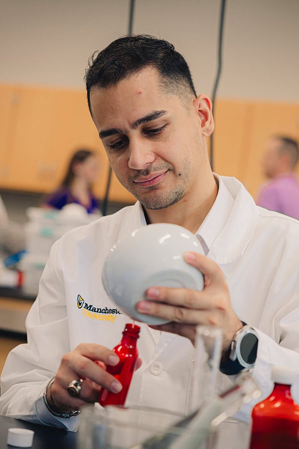 A male student in the pharmacy lab is carefully filling a red bottle.