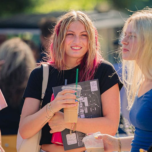 A female student with pink hair holds a coffee during Week of Welcome at MU