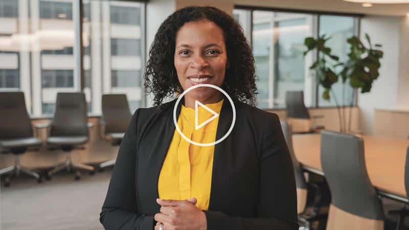 Alicia Baird sits in a boardroom - a play button indicates that a video can be played by clicking or tapping this image.