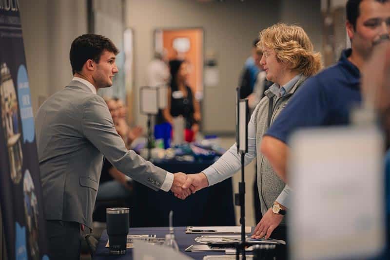 2 young men shake hands at the annual student symposium