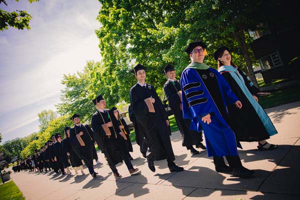 graduates march together led by Dr Lucas Dargo in a blue gown
