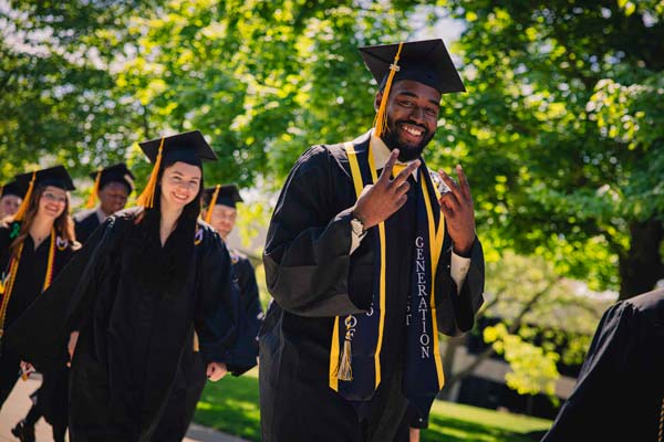 A graduate holds up 2 peace signs with his hands.