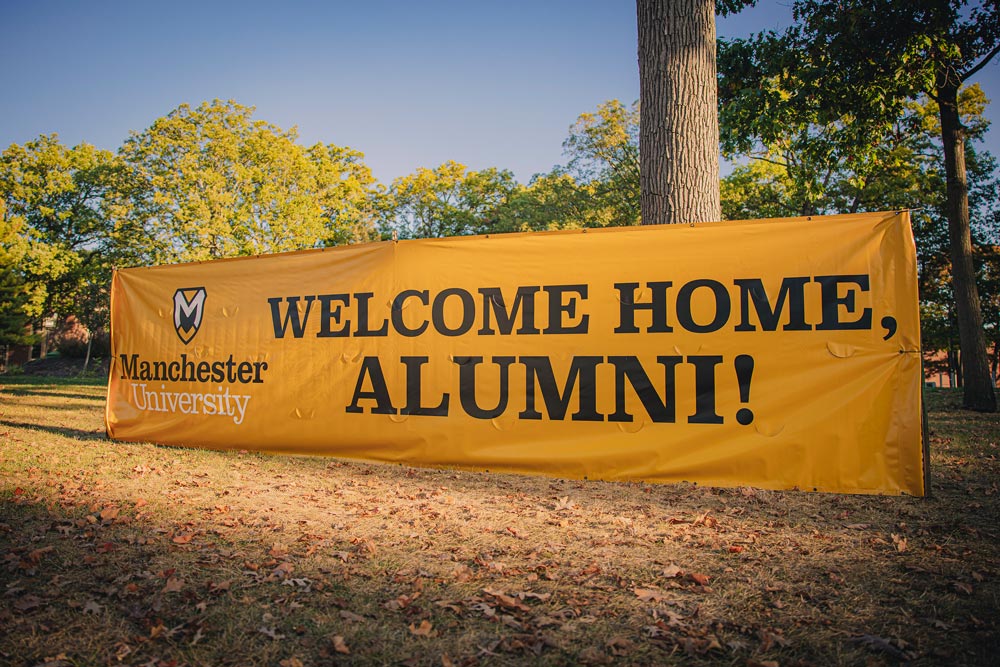 A Banner reads "Welcome Home Alumni" at the entrance to Manchester University.