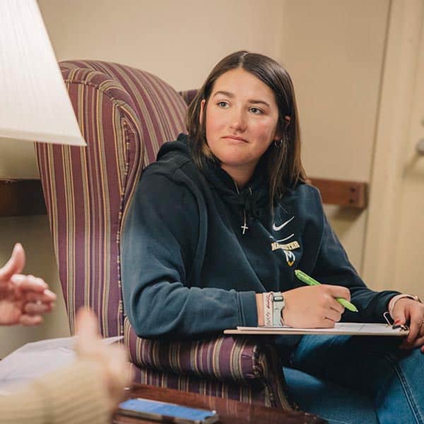 Sitting in a red striped chair a female student from Manchester University takes notes.