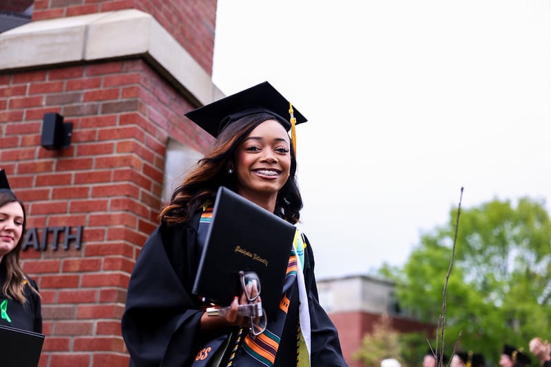 A female woman of color celebrates with her degree under the chime tower.