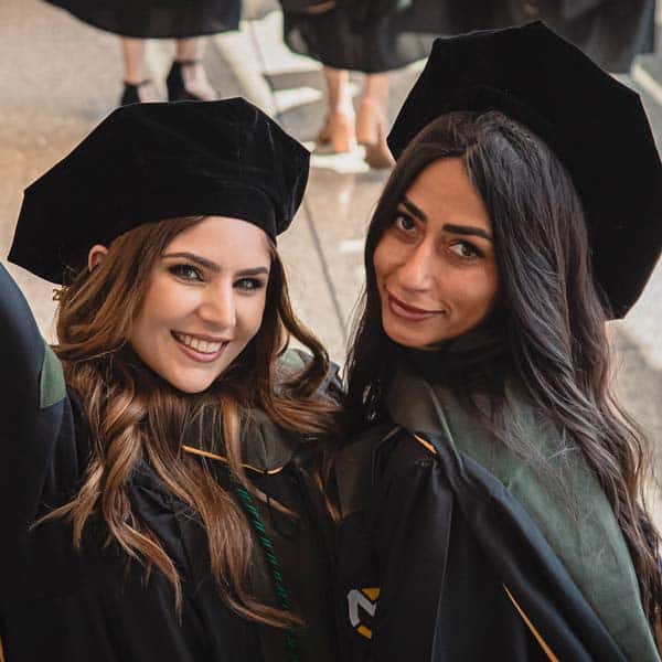 2 female students celebrate together in a photo after receiving their hoods at graduation for Pharmacy