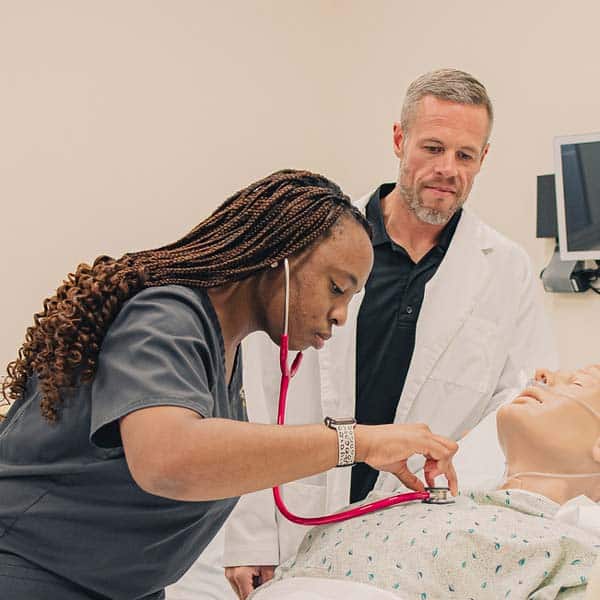 A Manchester University ABSN (nursing) student performs an exam using a pink stethoscope