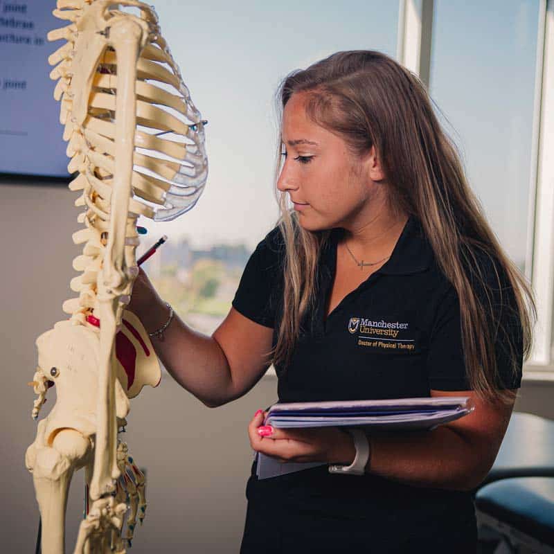 female student examines a skeleton and verifies data using a clipboard.