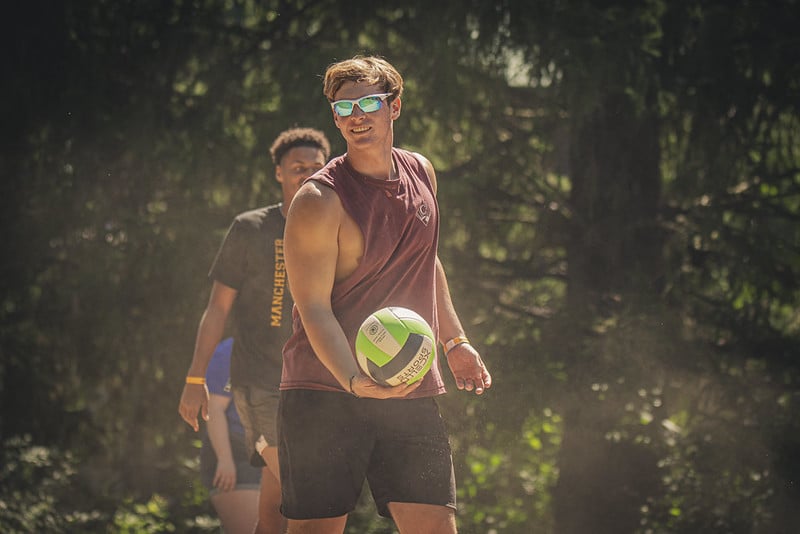 A young man holds a volleyball at the beach volleyball sandpit.