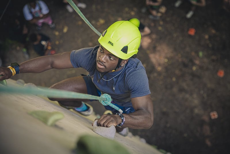 MU Student, Christian, climbs the wall at Camp Mack wearing a neon helmet and harness.
