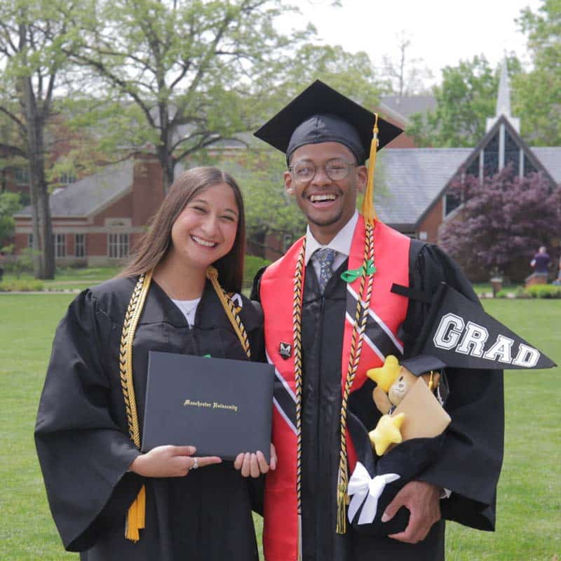 2 MU grads post ceremony celebrate with the chapel in the background. 