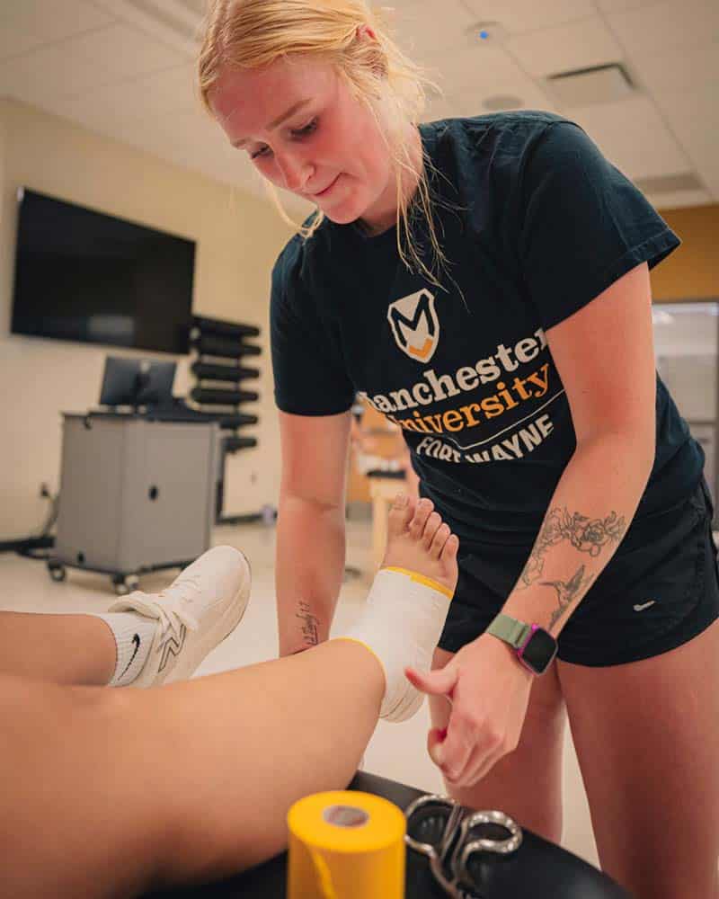 MATPrePro Femal MAT student wraps an ankle with yellow/gold tape.