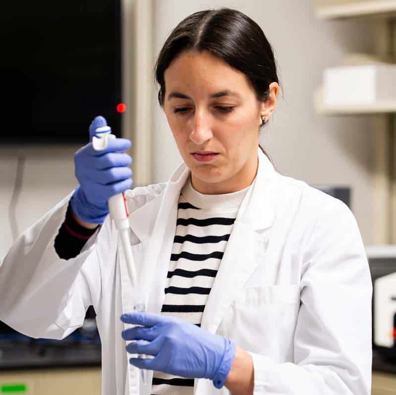 Female MU student uses a piping tool during a lab while wearing a lab coat.