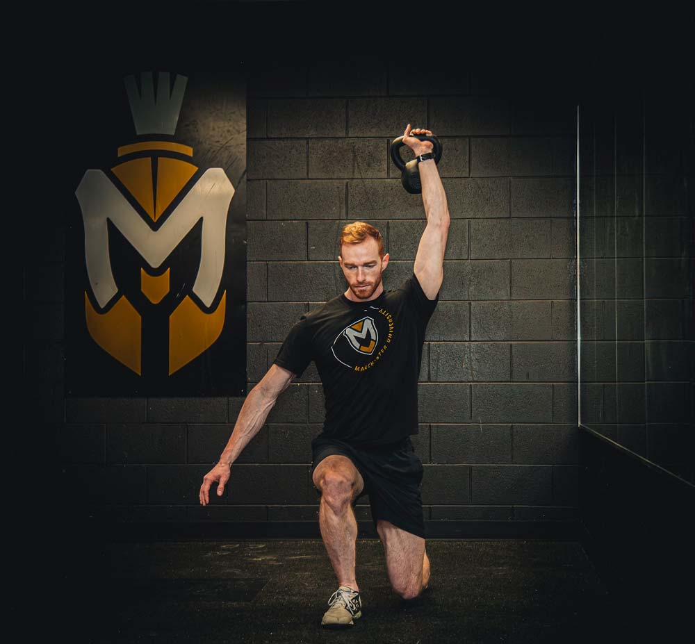 A student practices the proper technique for a kettle bell in front of the MU Spartans logo.