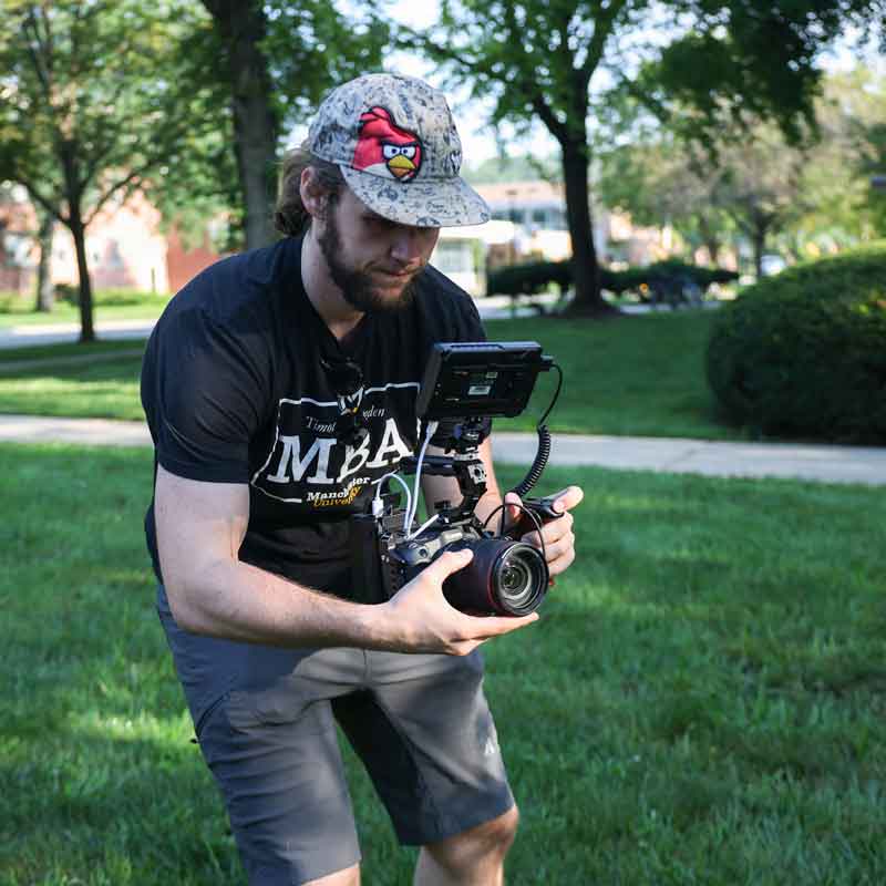 MU Grad films for Manchester Marketing while wearing an MBA shirt.